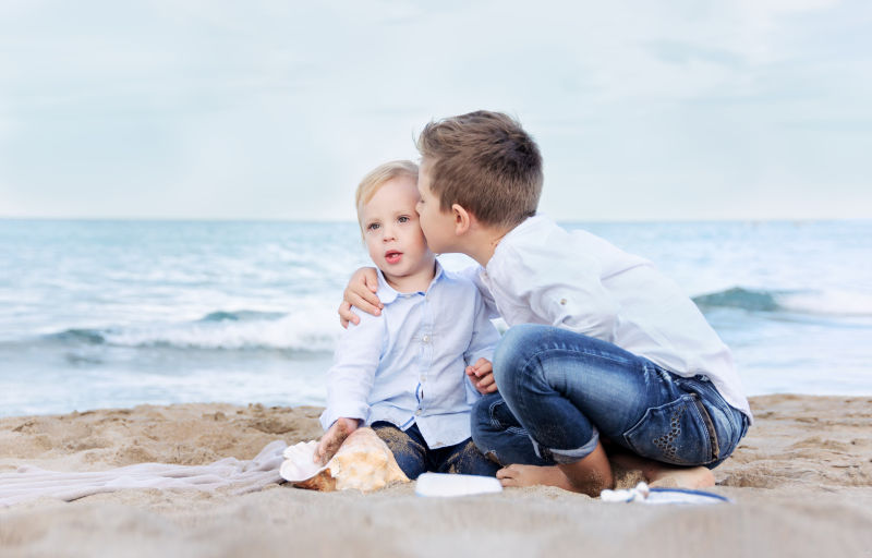 哥哥吻了坐在沙滩上的弟弟