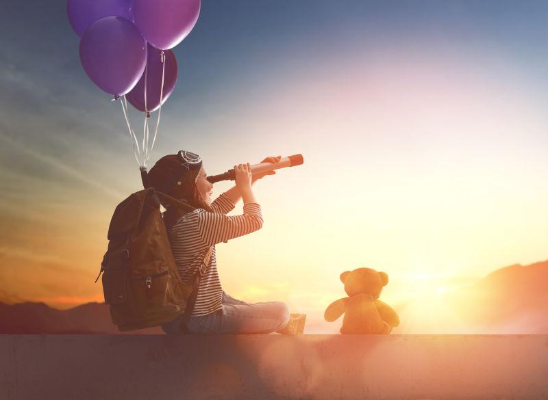 带背包和气球的年轻旅行孩子用望远镜看日落
