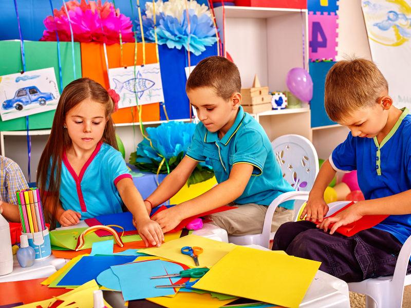 一群孩子在幼儿园的桌子上做彩色纸手工