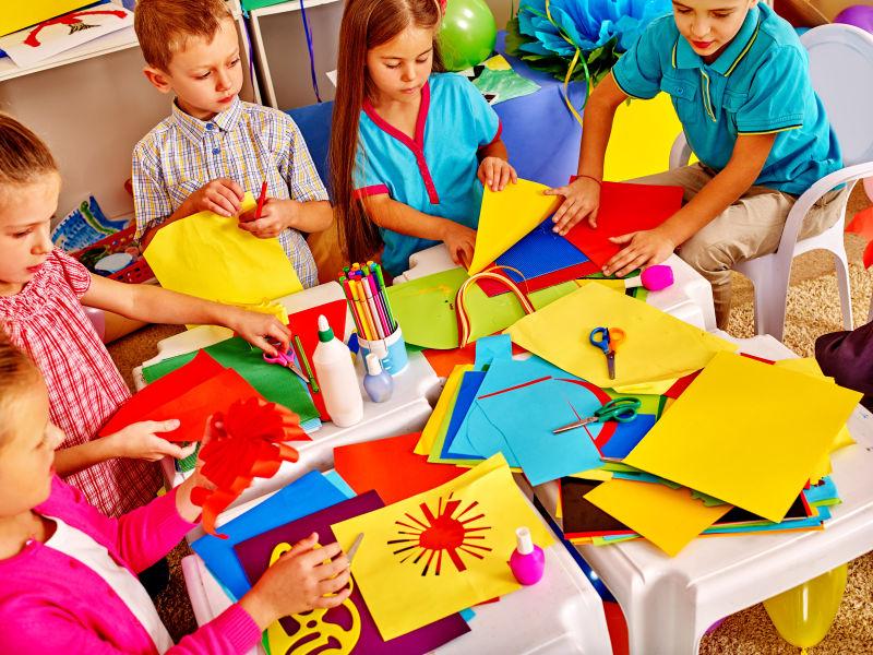 拿着彩色纸绘画和做手工的幼儿园的孩子们