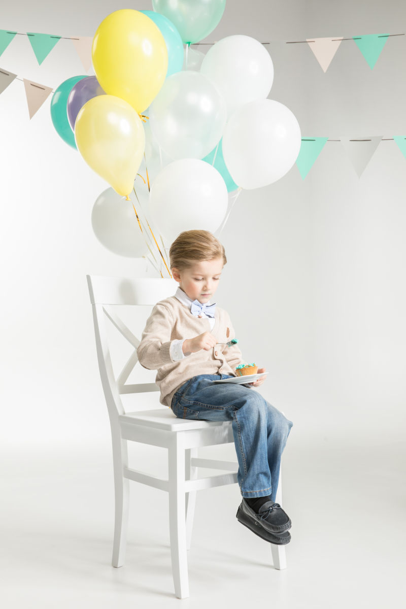 可爱的小男孩坐在绑着气球的椅子上吃甜点