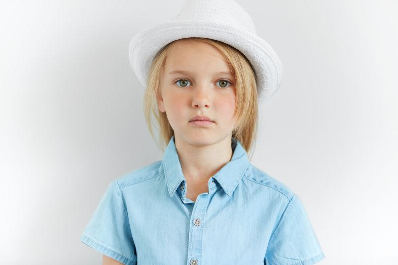 穿着蓝色衬衫带着白色帽子的金发小女孩