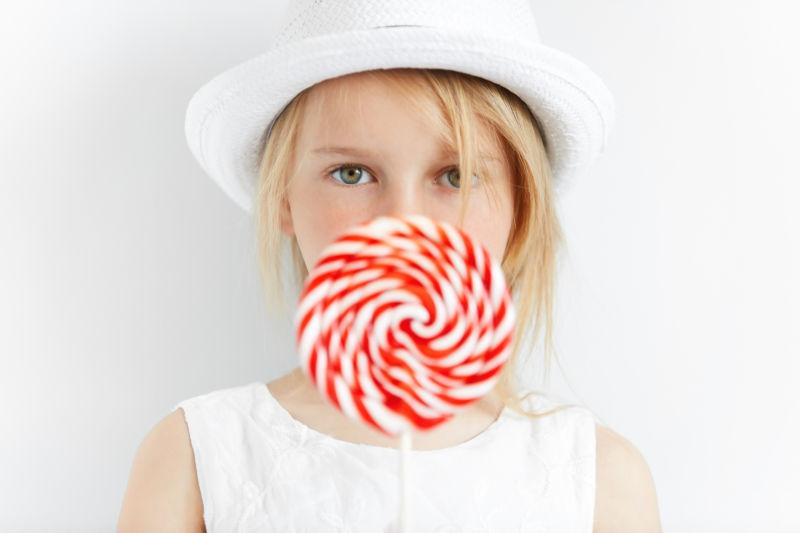 带着白色帽子的小女孩拿着一个棒棒糖