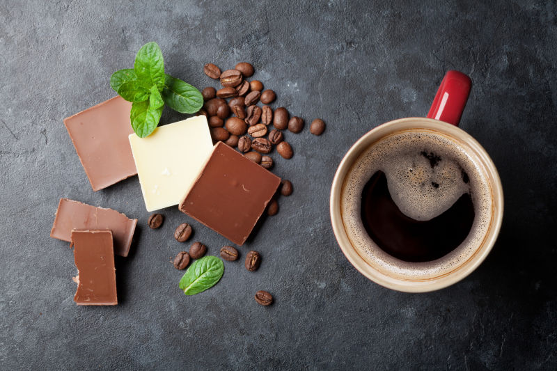 一杯黑咖啡旁放着巧克力和咖啡豆