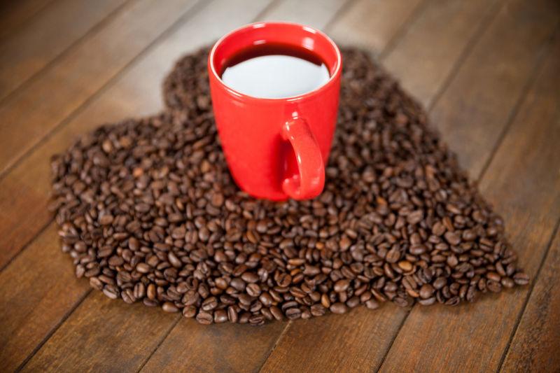 木制咖啡桌上有心形咖啡豆和红色咖啡杯里的咖啡