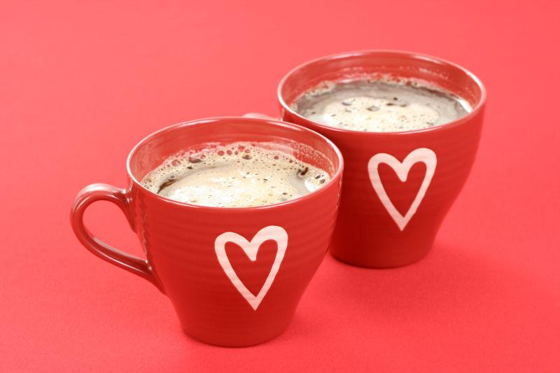 桌面上的两杯画着爱心的红色咖啡杯