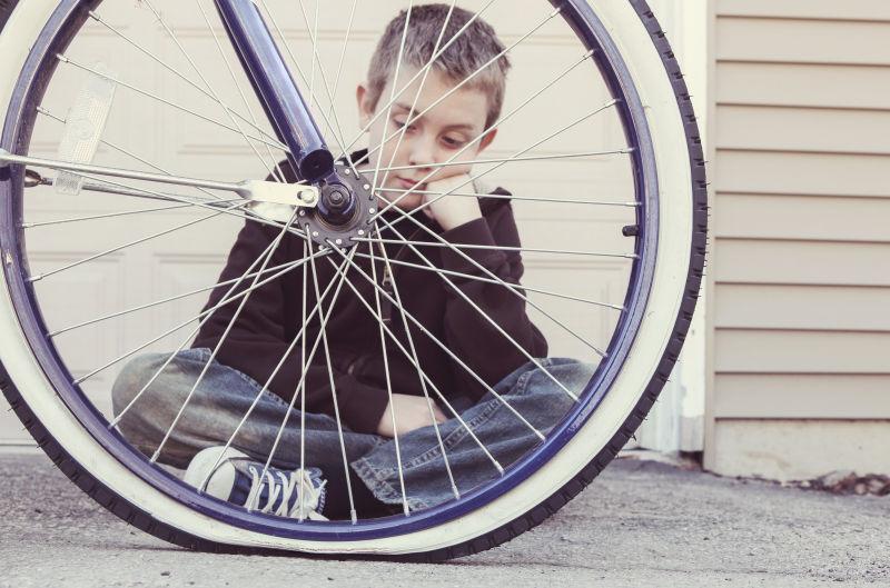 悲伤的男孩看着他的自行车轮胎