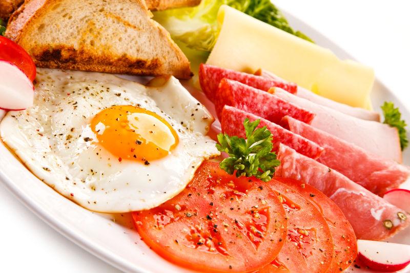 放在白色盘子里的鸡蛋面包和番茄火腿早餐美食