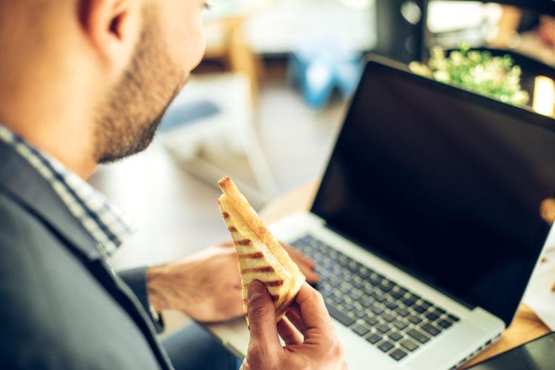 男子在笔记本电脑上吃三明治