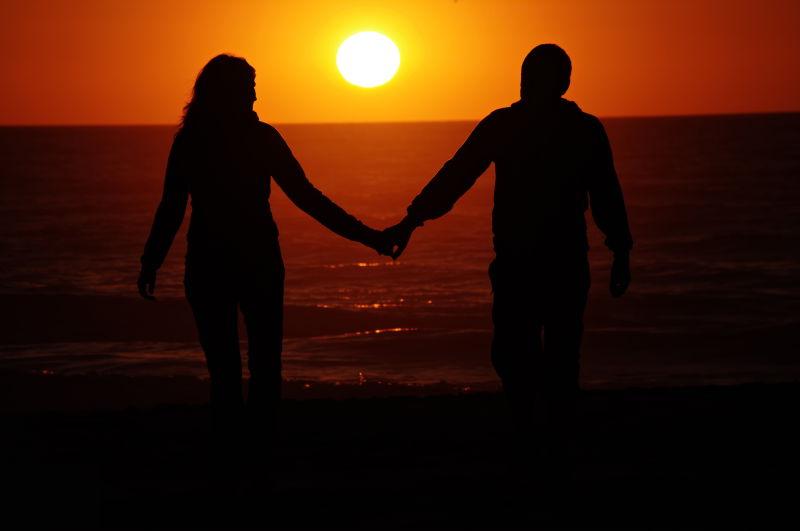 夕阳下海滩上手拉手的浪漫夫妇剪影