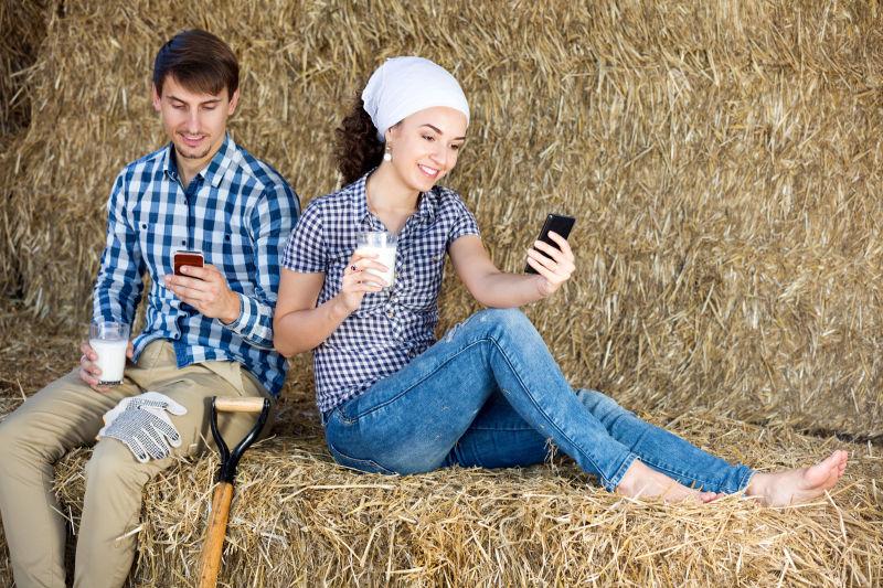 积极的男人和女人在干草看着电话和享受新鲜的牛奶