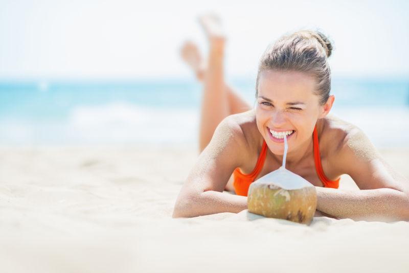 躺在沙滩上喝椰子奶的年轻女子