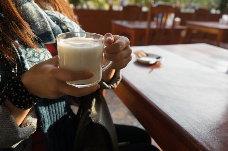 坐在木桌上的女人抱着一杯牛奶