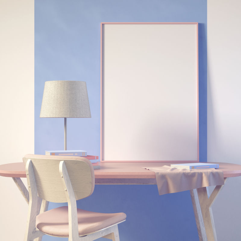 蓝色墙壁旁的粉色椅子和办公桌上的空白画框
