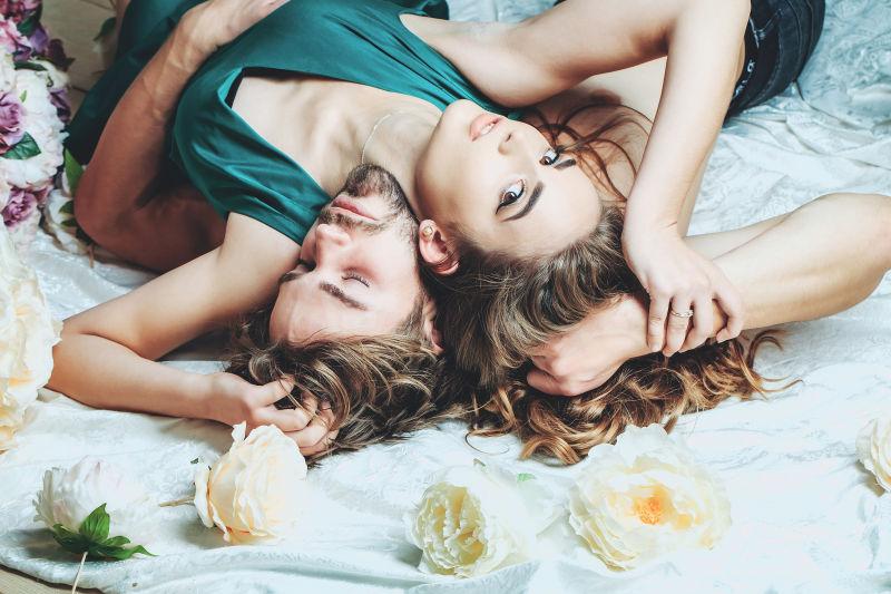 性感情侣躺在有鲜花的白色床单上