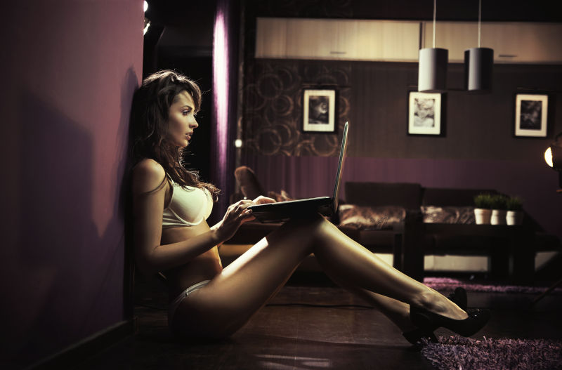 坐在墙边使用笔记本电脑的性感美女