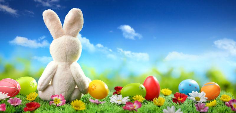蓝天白云下草地上的复活节彩蛋和毛绒玩具兔子