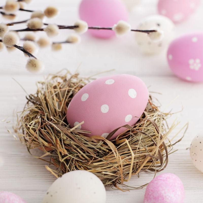 白色桌上的草窝里的粉色复活节彩蛋