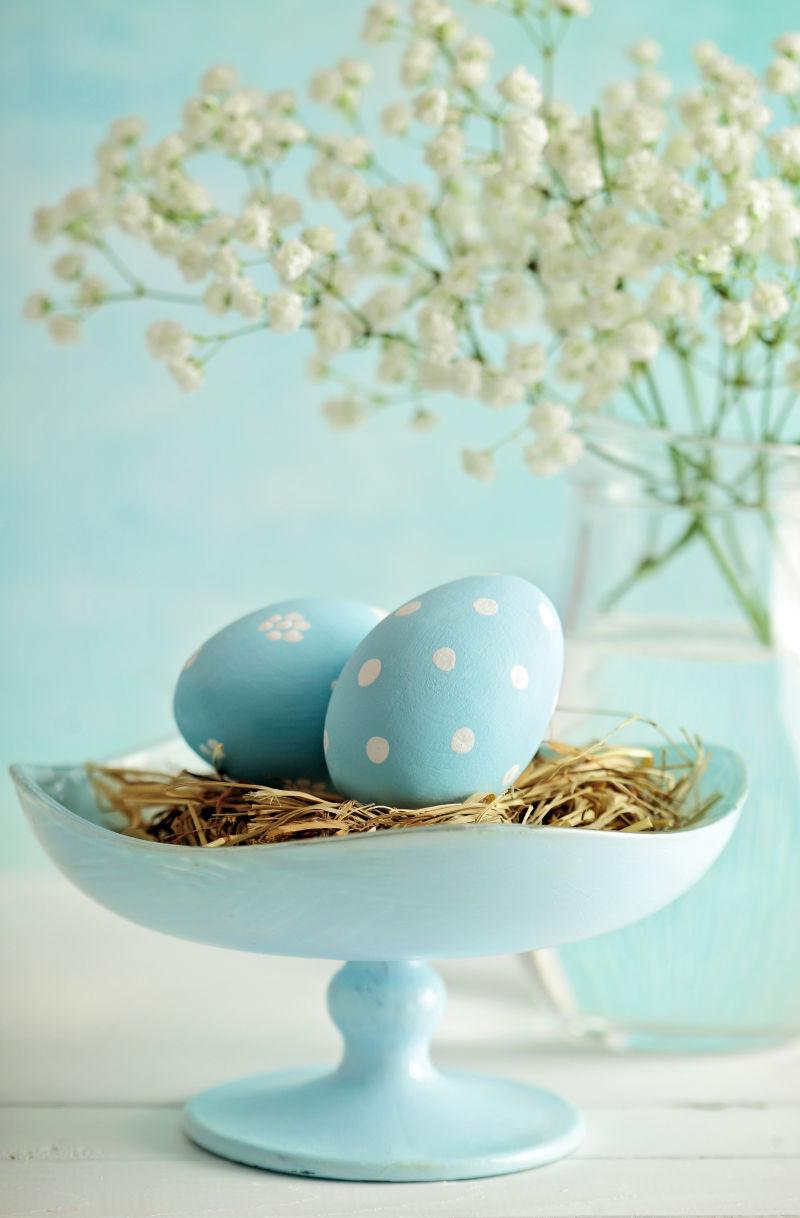 放着白色满天星的桌上放在草窝里的蓝色复活节彩蛋