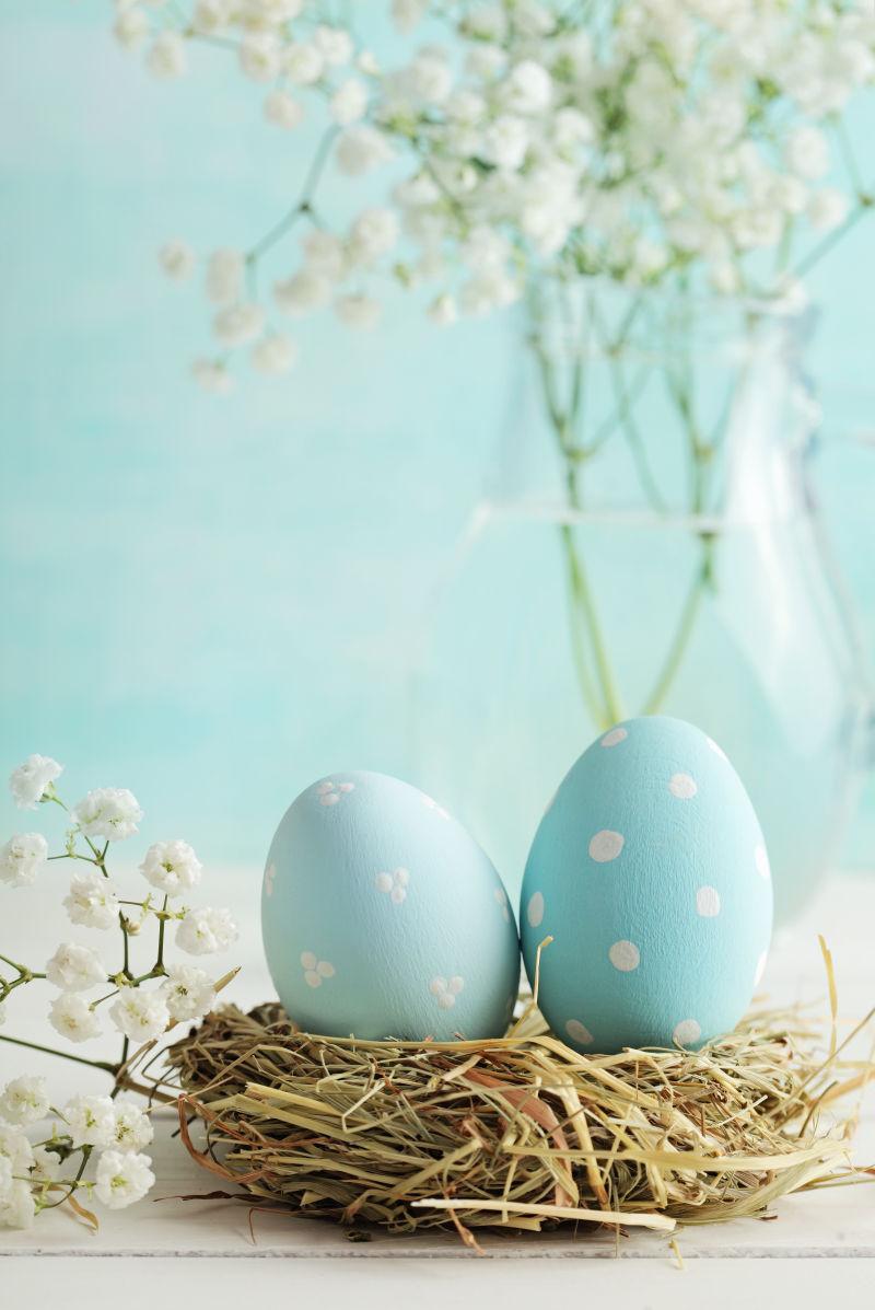 蓝色背景下白色桌子上的白色满天星和鸟窝上的复活节彩蛋