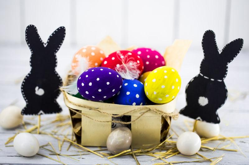 白色桌上的木筐里的复活节彩蛋和黑色兔纸