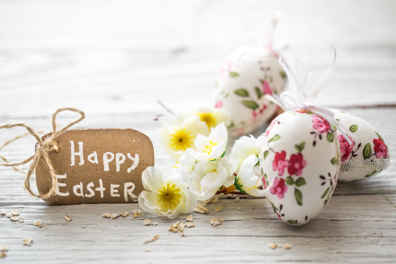 白色木纹理桌上的复活节花朵彩蛋和祝福卡片