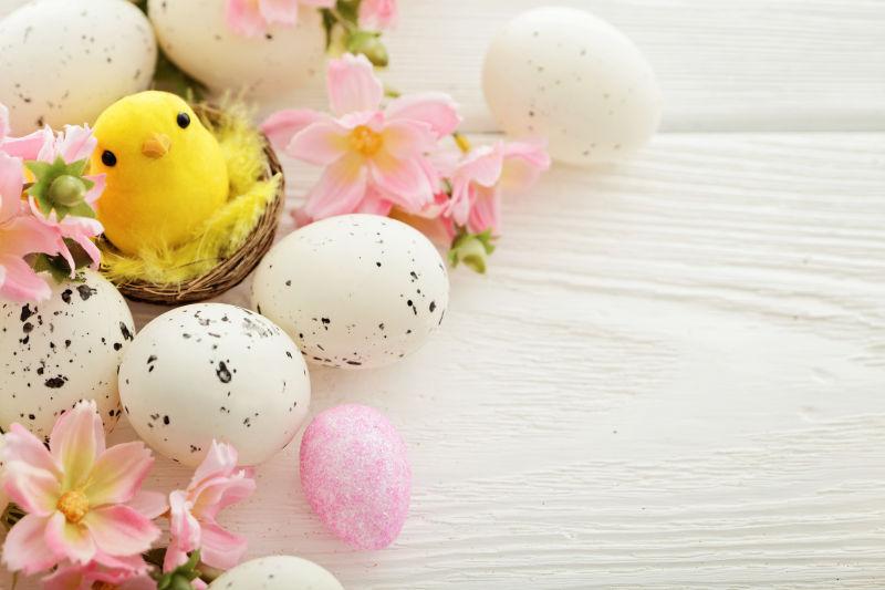 摆满粉色花朵的白色桌上的复活节彩蛋和小黄鸡