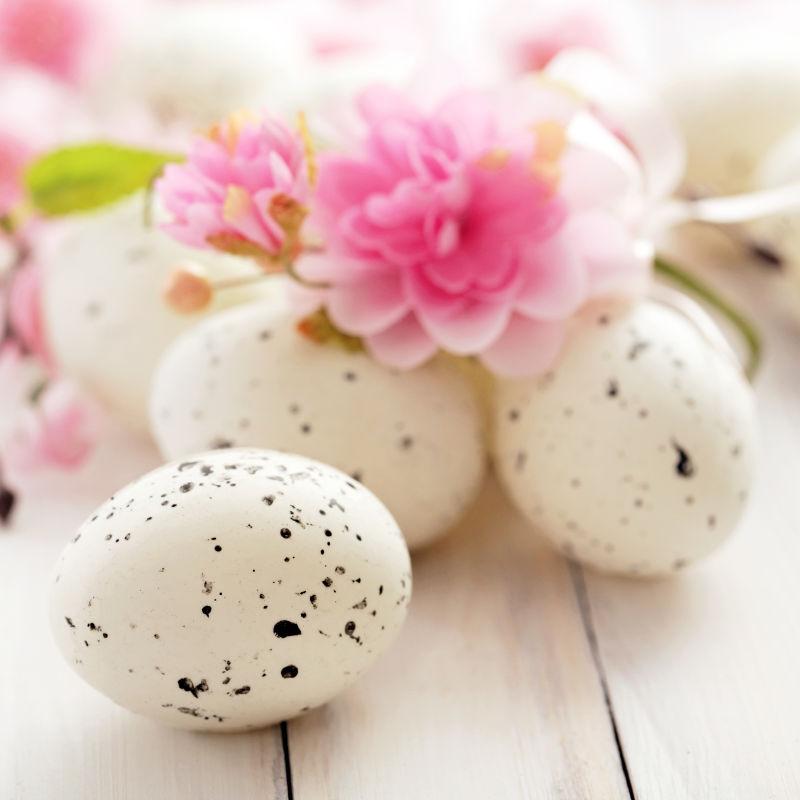 白色木桌上的白色的复活节彩蛋和粉色的花朵