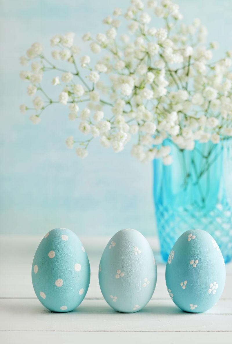 白色背景上的蓝色复活节彩蛋和玻璃瓶子里的白色满天星