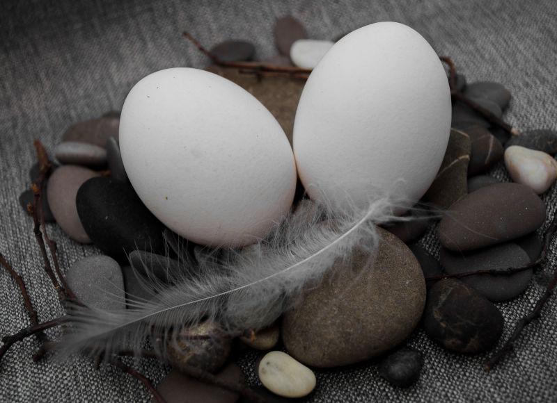 灰色桌上的石头和羽毛上的两只白色鸡蛋
