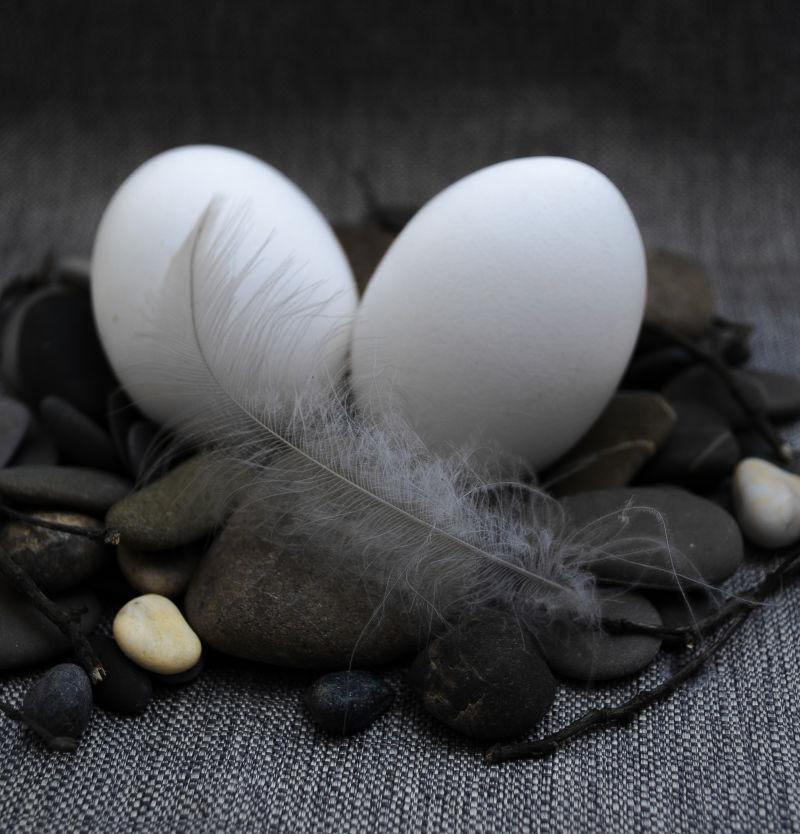 灰色背景上的黑色亚麻布上的复活节彩蛋和一片羽毛