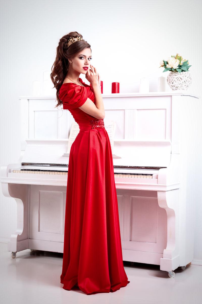 站在白色钢琴前穿红色礼服的女人