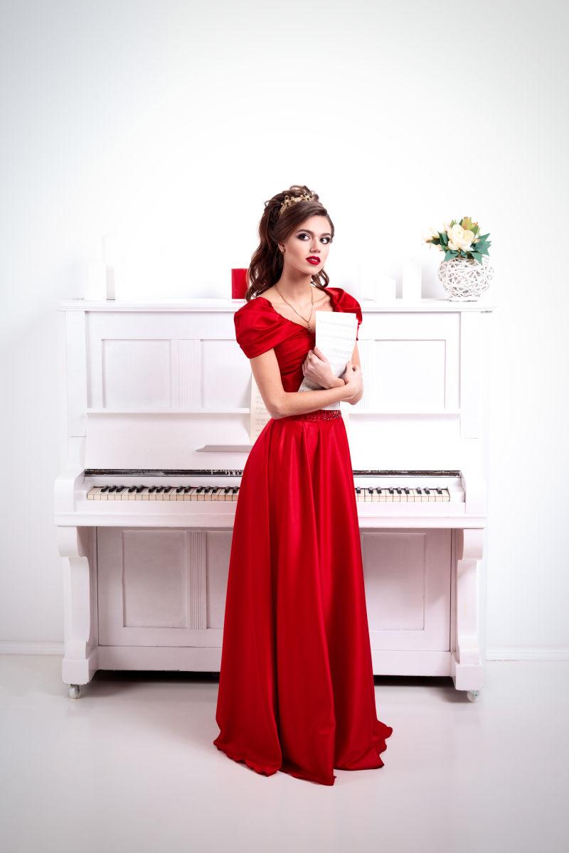 穿红色长裙的女人站在白色钢琴前