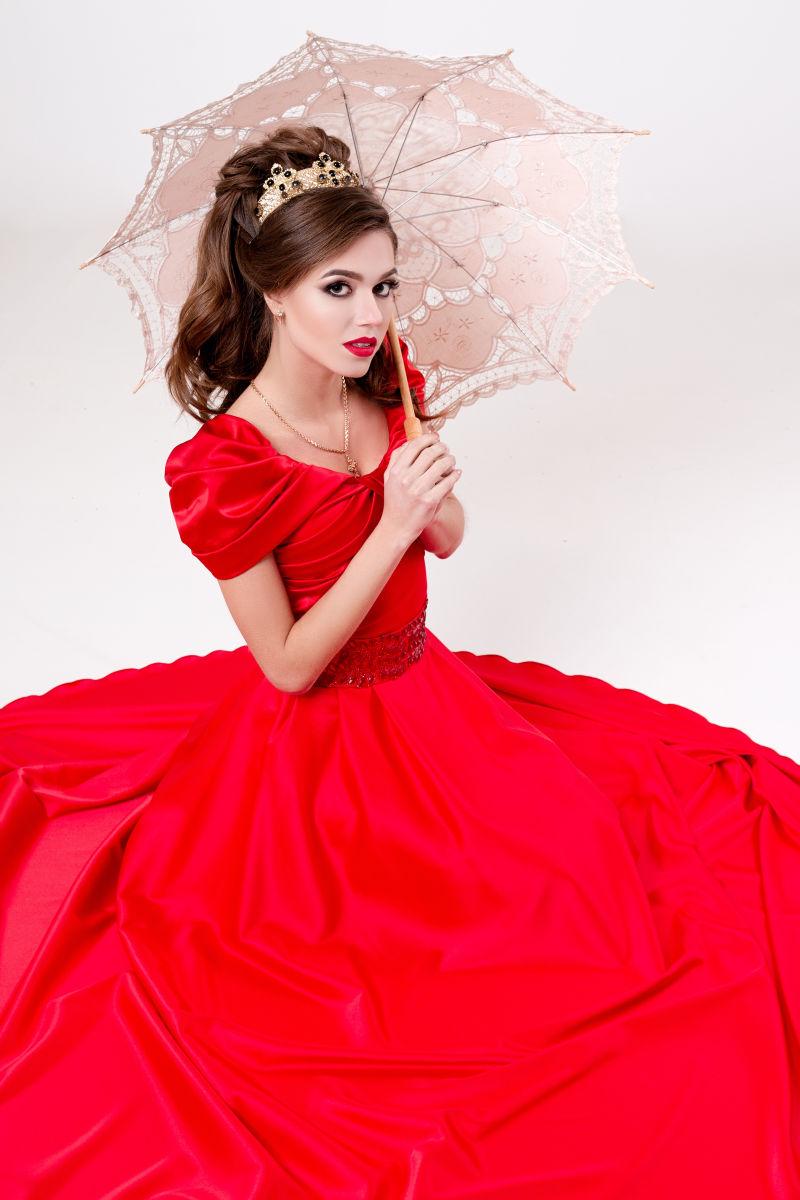 白色背景中打着古董伞坐在地板上穿红裙子的女人