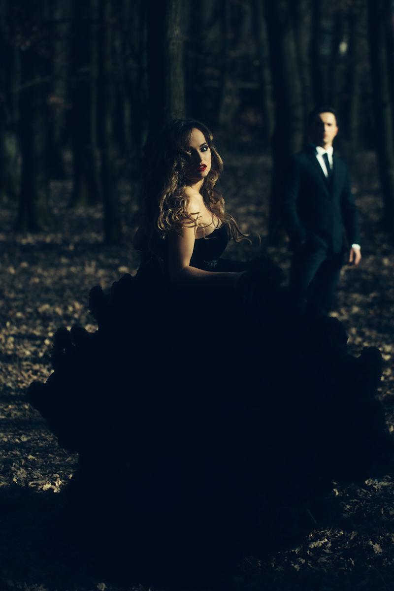 身着黑色西装的英俊男子和身穿优雅的礼服的性感女郎在森林中