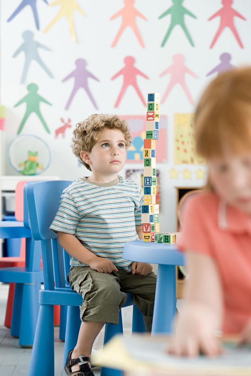 坐在教室内的桌子前玩积木的小男孩