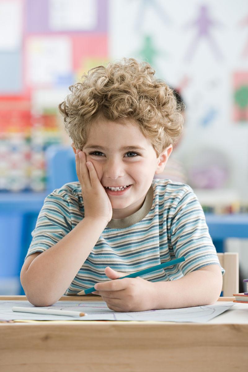坐在教室的课桌前微笑的男孩