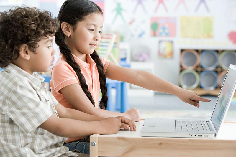 坐在教室内使用笔记本电脑的男孩和女孩