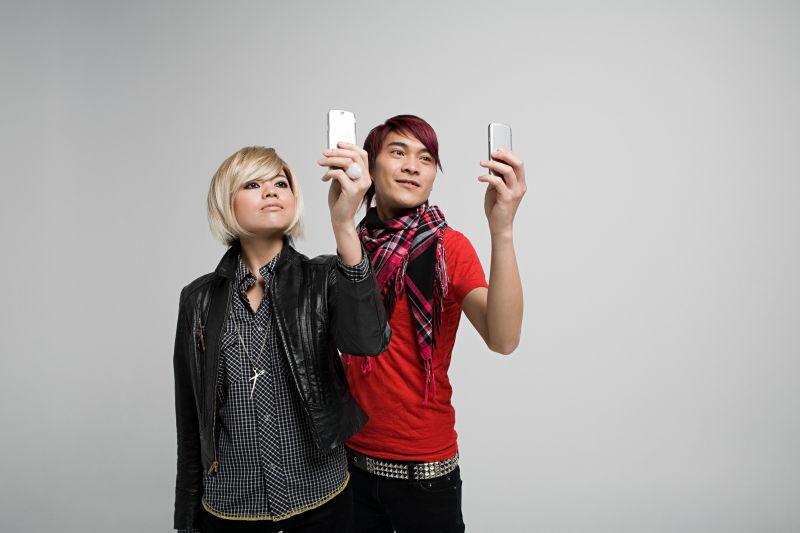 灰色背景下拿着手机自拍的年轻亚裔情侣