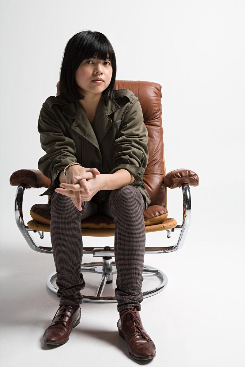 白色背景下坐在扶手椅上的年轻亚裔女子