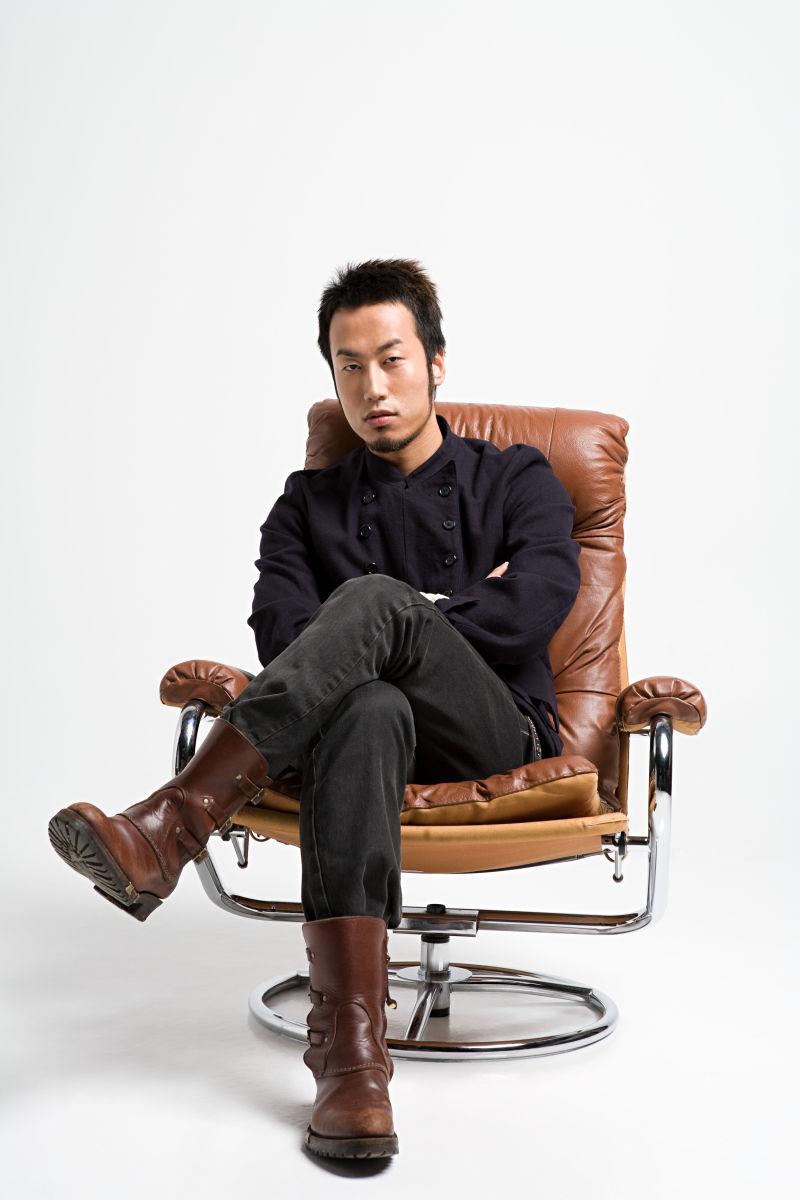 白色背景上坐在棕色扶手椅上的亚裔年轻男子