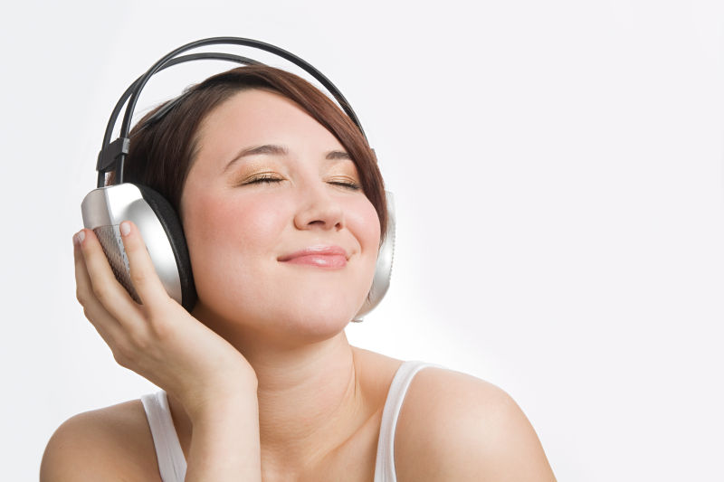 一个迷人的黑发女郎在白色背景下聆听音乐
