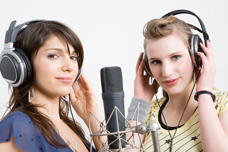 话筒前戴着耳机的两个年轻女歌手