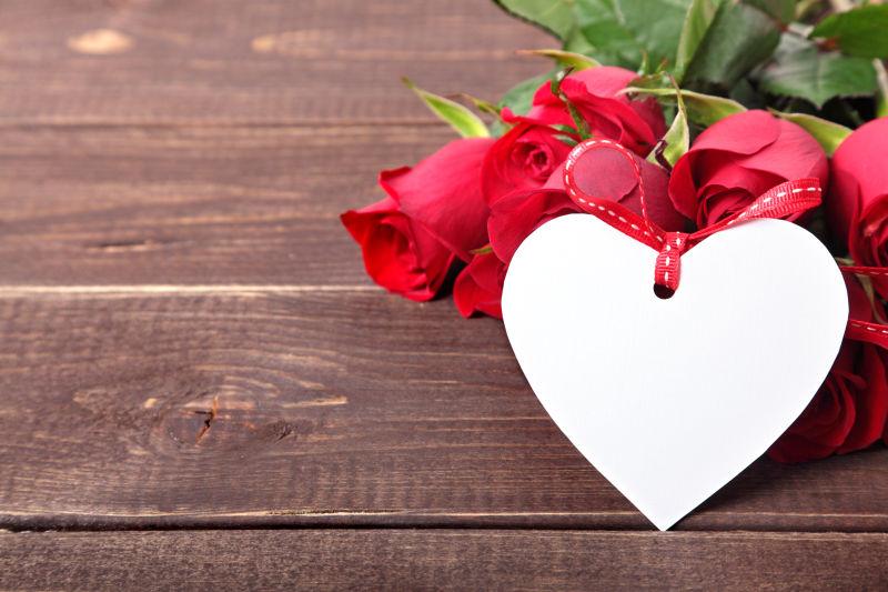 木板上的情人节红玫瑰和白色纸心