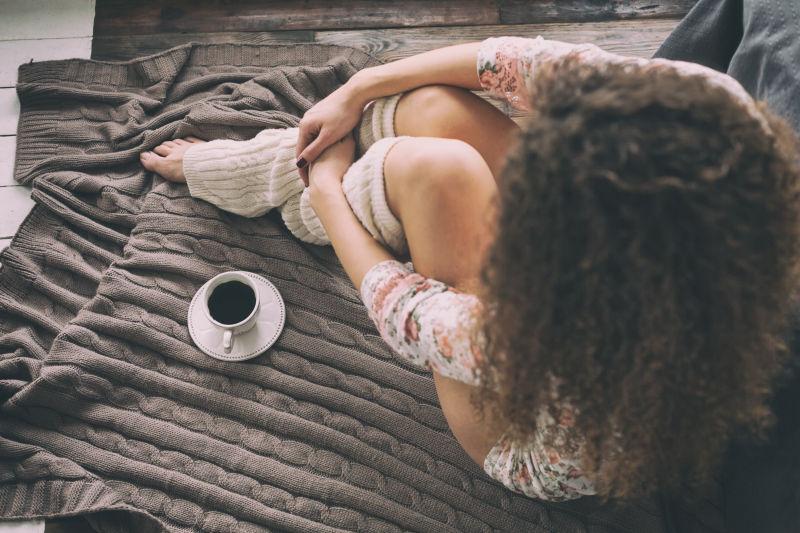 年轻的高加索女孩和咖啡杯坐在床旁的地板上