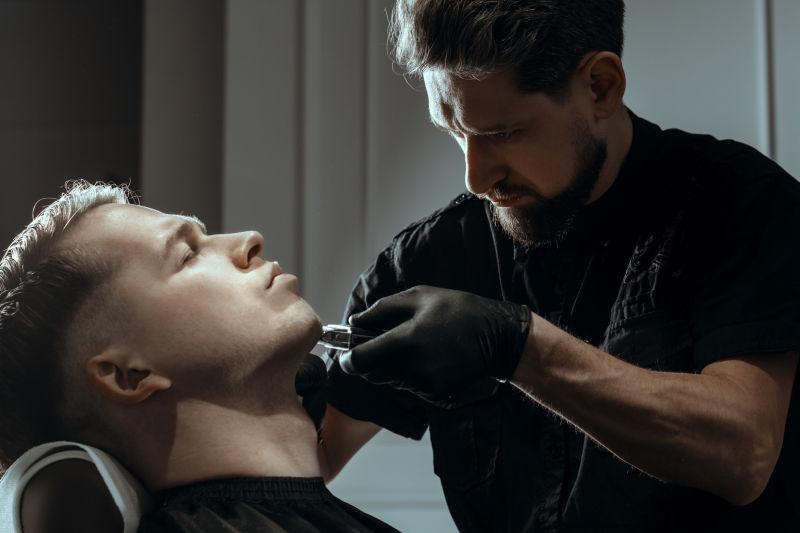 男性理发师在为男性顾客修剪胡须