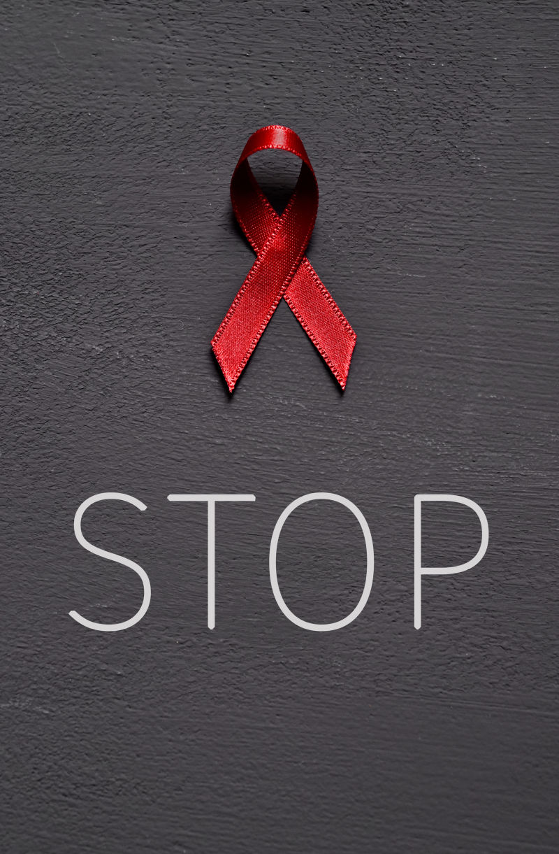 抗击艾滋病的红丝带和暗灰色表面上的“停止”字