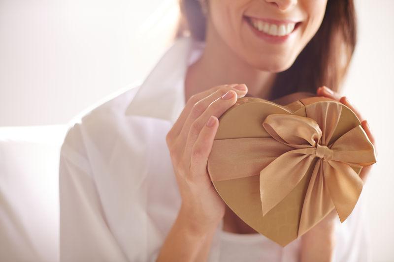 微笑的女性紧抱着心形礼品盒