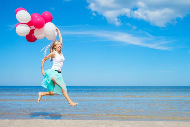 在海边手拿气球跳跃的美女