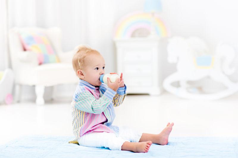可爱的小男孩坐在蓝色的地板从一个瓶子里喝牛奶上